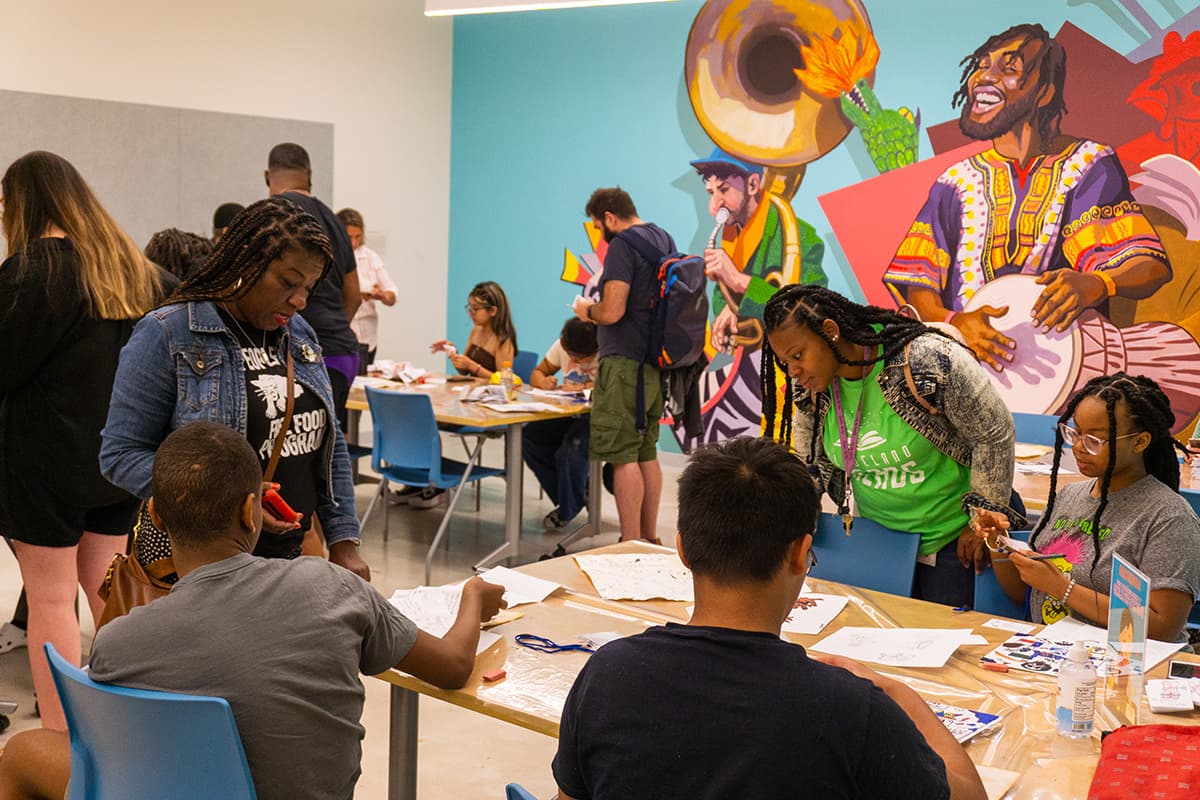Adults and students standing around and looking at art on the tables throughout the room